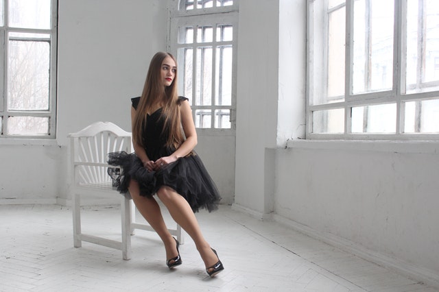Dívka v černých tylových šatech sedící na židli v prázdném pokoji