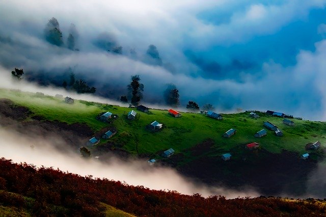 krásná příroda, louka v kopci, na ní několik objektů, v popředí mlha a za nimi mlha a lesy